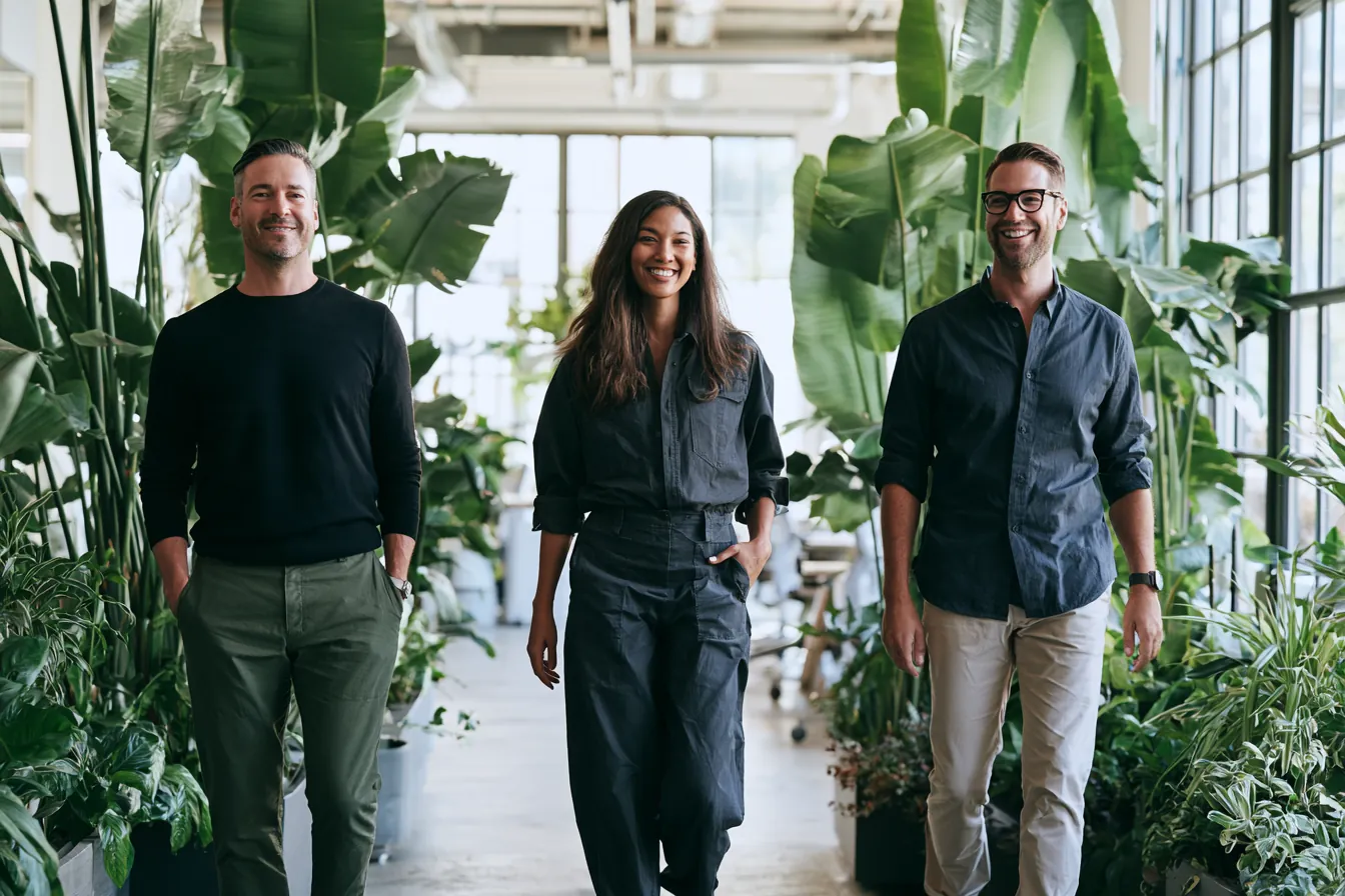 Three teammates, mixed ages walking together through a bright plant-filled coworking space (Makwa Loans)