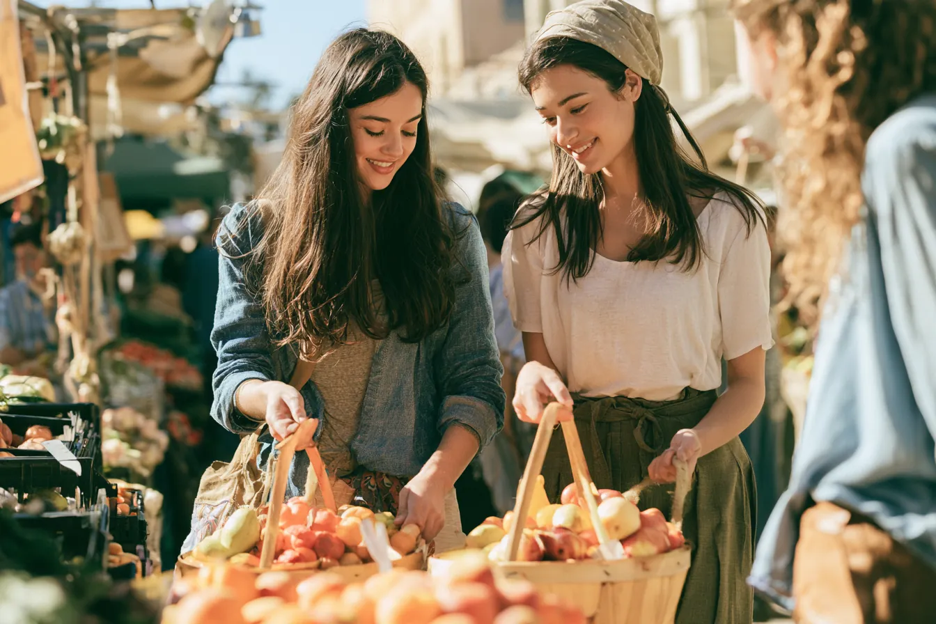 Two friends in their 20s strolling between produce stalls comparing baskets of fruit (Makwa Loans)
